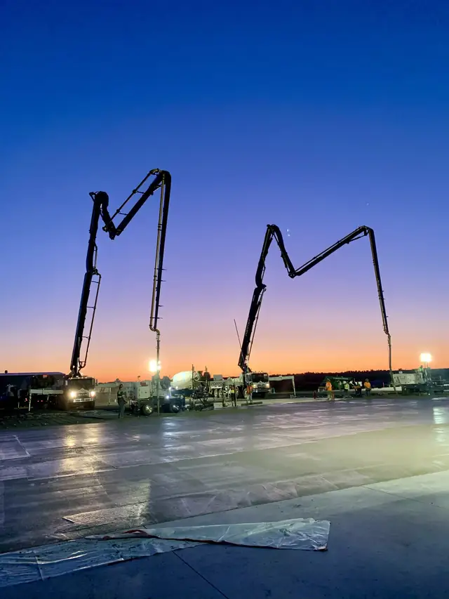 Two Poppoff boom pumps silhouetted against a sunrise over a fresh slab