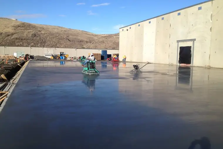 Power trowels working a glassy fresh slab beside a new tilt-up wall at Columbia Reach in Yakima
