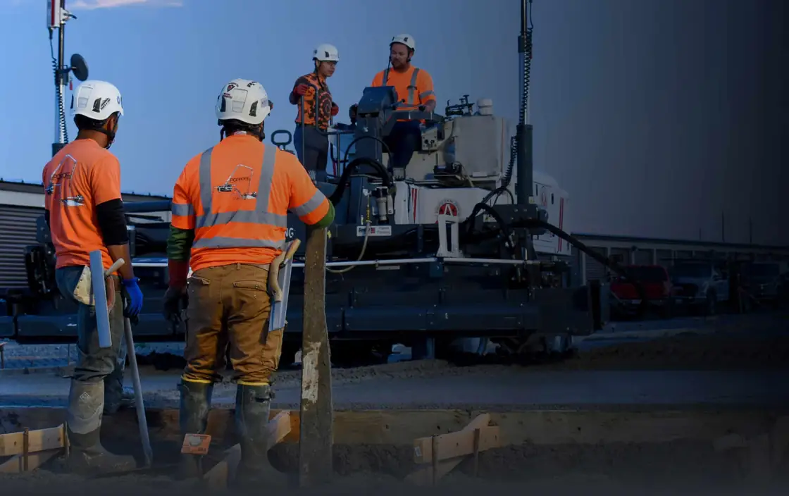 Poppoff crew in hard hats and hi-vis working beside a laser screed on a slab