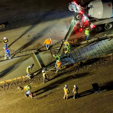 A night pour with the crew raking fresh concrete beside a mixer truck